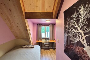 A bedroom with a bed, a desk, and a chair. There is a window with curtains, a wall with a tree painting, and a ceiling with wooden beams. - Algonquin HappyForest Cottage-Canadian Highlander's Eco-Log Home at Kushog Lake (Algonquin Highlands)