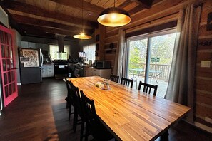 Una mesa de comedor de madera con sillas, una zona de cocina con electrodomésticos y un ventanal con vistas al exterior.