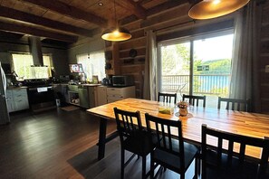 A kitchen with a wooden table and chairs, a stove, and a view of the outdoors through a window. - Algonquin HappyForest Cottage-Canadian Highlander's Eco-Log Home at Kushog Lake (Algonquin Highlands)