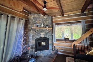 Una sala de estar acogedora con chimenea de piedra, vigas de madera, una escalera y un ventanal grande.