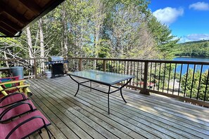 A wooden deck with a glass table and chairs, overlooking a lake and forest. - Algonquin HappyForest Cottage-Canadian Highlander's Eco-Log Home at Kushog Lake (Algonquin Highlands)
