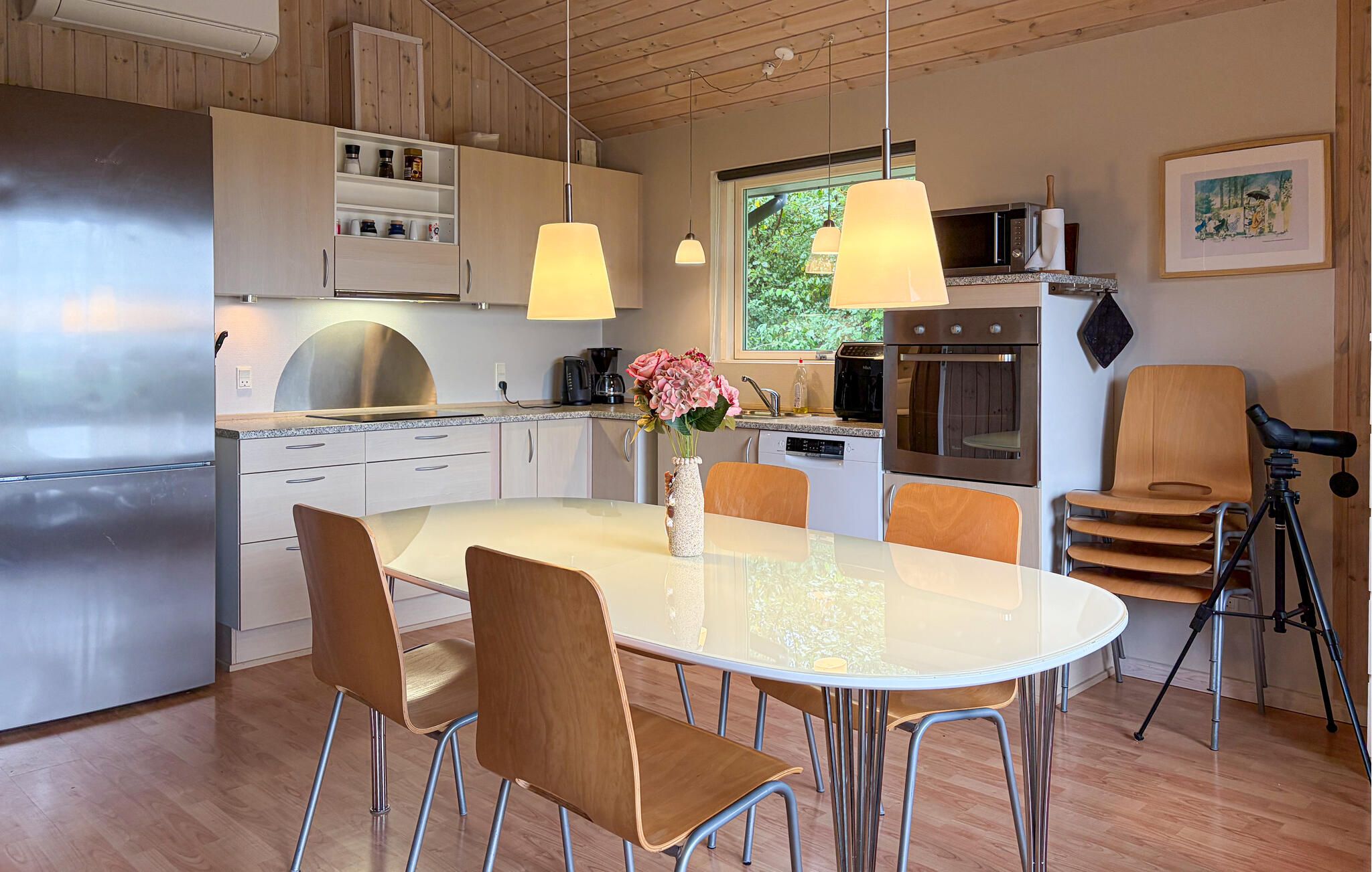 Een moderne keuken met een centraal eiland, roestvrijstalen apparatuur, hangende verlichting en een eethoek met stoelen en een tafel.