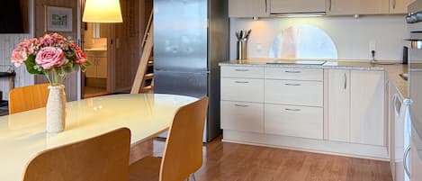 A modern kitchen with a stainless steel refrigerator, wooden cabinets, and a dining area with a white table and chairs.