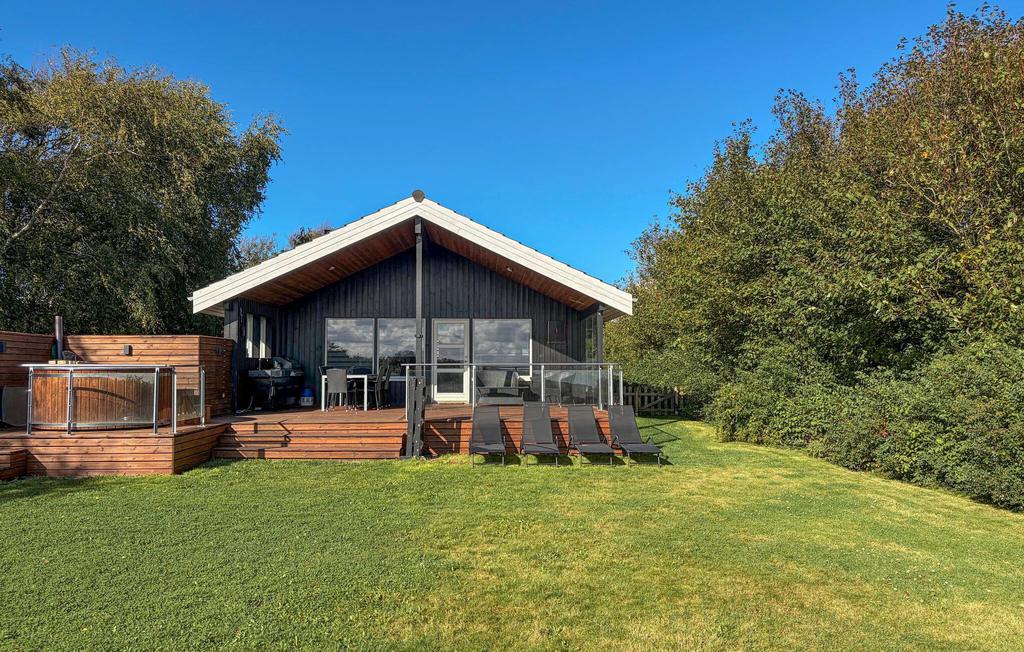 A modern wooden cabin with a deck, outdoor seating, and a large window.