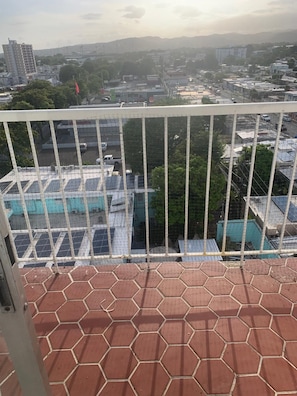 A balcony with a view of a cityscape, including buildings and a distant mountain range. - Perfect 1-bedroom apartment with AC in charming Ponce,Secure Free Parking (Ponce)