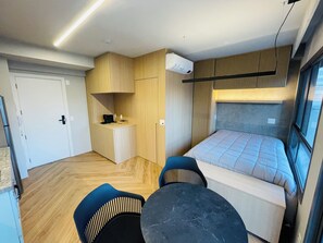 Quarto de hotel compacto com uma cama, uma pequena escrivaninha, uma cadeira e uma mesa.