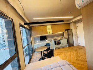 A modern hotel room with a large window, a bed, a small dining table, and a kitchenette. - Studio Nex One Itaim (São Paulo)
