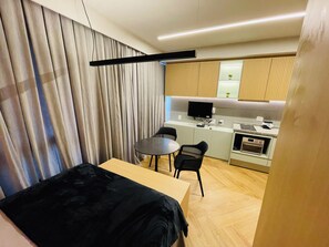 A compact hotel room with a bed, a small desk, a chair, a television, and a kitchenette. - Studio Nex One Itaim (São Paulo)