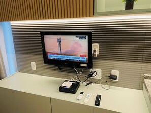 A television mounted on a wall with a remote control and a streaming device on a white surface below. - Studio Nex One Itaim (São Paulo)