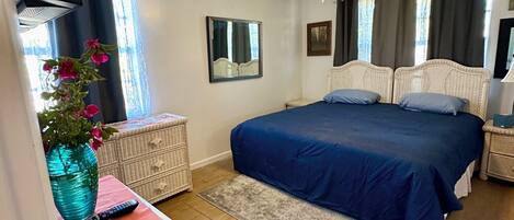 A bedroom with a bed, a ceiling fan, a dresser, a vase with flowers, and a window with curtains.