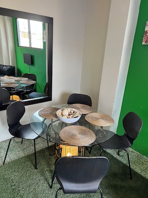 Ein runder Glastisch mit gewebten Tischsets, umgeben von schwarzen Stühlen, in einem Raum mit grüner Akzentwand und einem großen Spiegel.