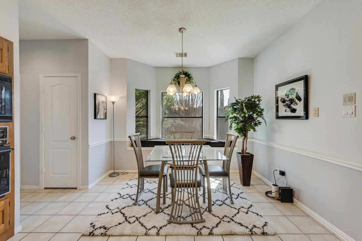 A dining area with a glass table, metal chairs, a chandelier, and a potted plant.