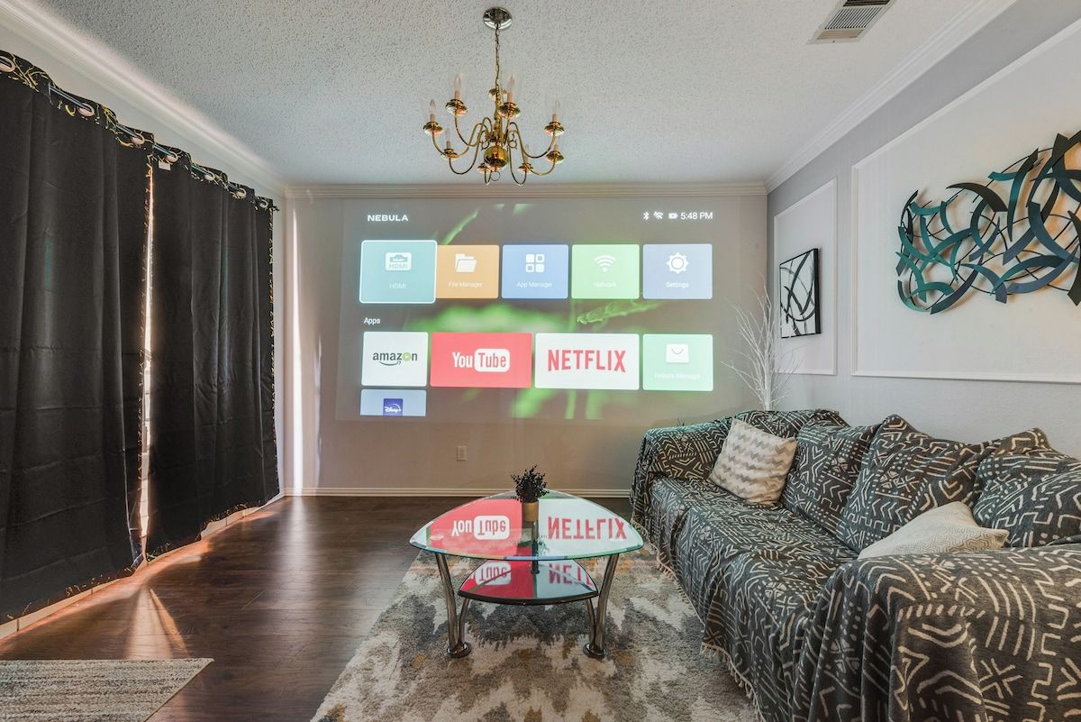 A living room with a modern chandelier, a sofa with patterned cushions, and a coffee table with a glass top.