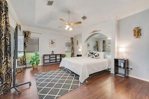 A bedroom with a bed, a ceiling fan, a desk, a chair, a small table, a plant, and a mirror. - Light-filled 6-bedroom furnished home, 3,300 sqft, monthly stays (Plano)