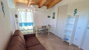 A living room with a brown sofa, a dining table with chairs, a white wall with a seahorse decoration, and a tiled floor. - Apartment just a few meters from the beach (Quartu Sant'Elena)