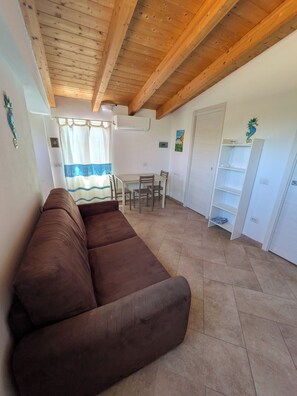 Een woonkamer met een bruine bank, een eettafel met stoelen, een witte muur met een decoratie van een zeepaard en een betegelde vloer.