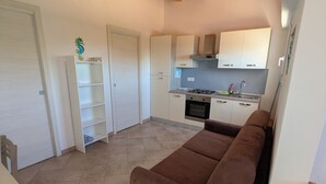 A compact living space with a brown sofa, a dining table, and a kitchenette. - Apartment just a few meters from the beach (Quartu Sant'Elena)