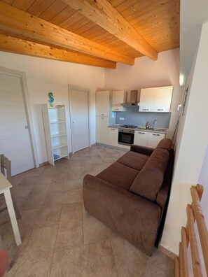 Een compacte leefruimte met een bruine bank, een eettafel en een kitchenette.
