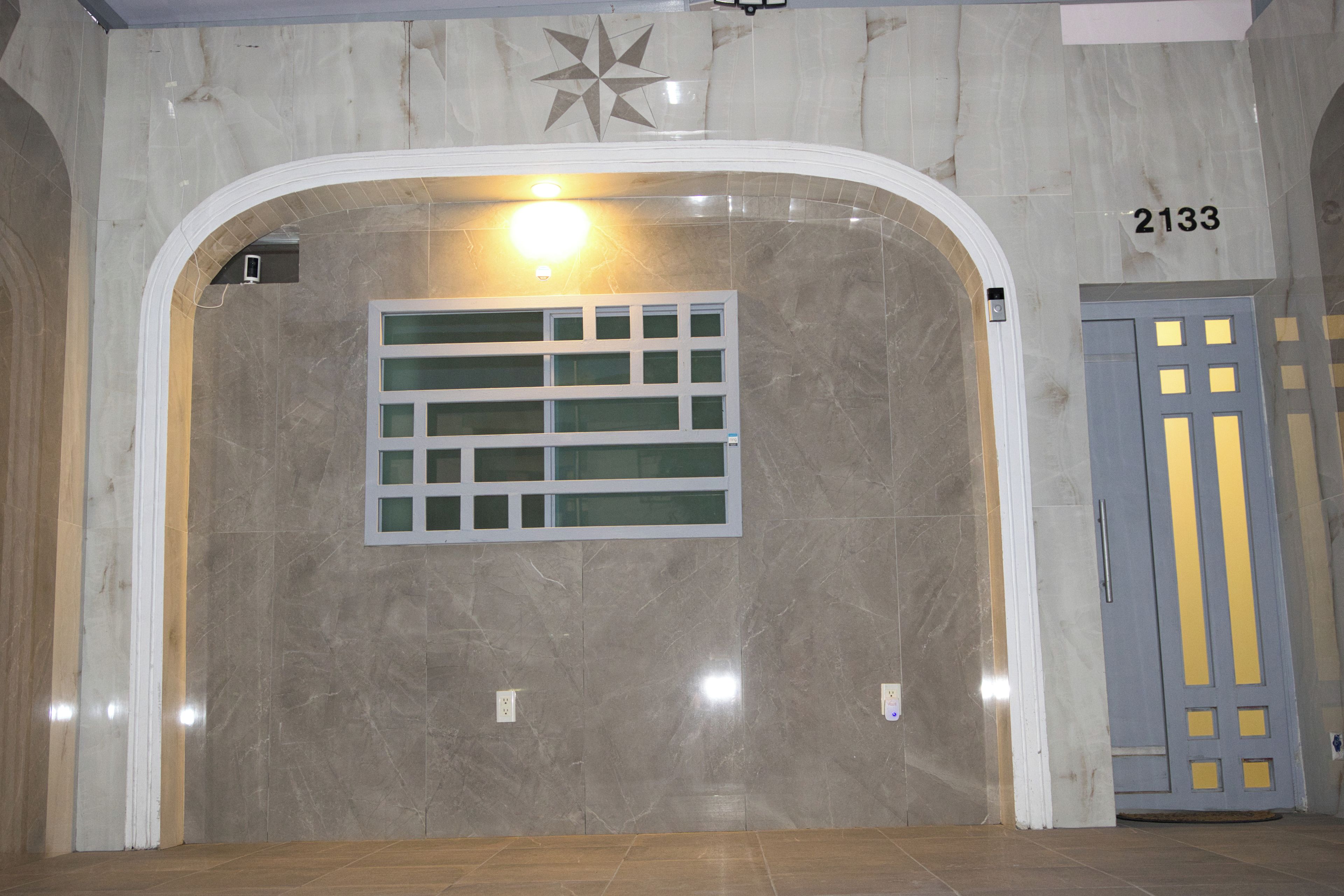 An interior hallway with a marble wall, a star-shaped decoration, a light fixture, and a door with a number sign.