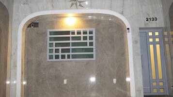 An interior hallway with a marble wall, a star-shaped decoration, a light fixture, and a door with a number sign.