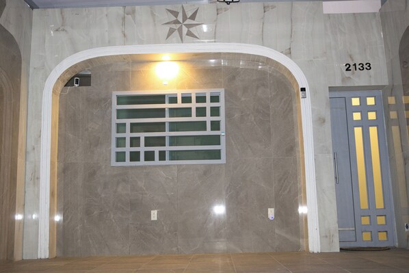 An interior hallway with a marble wall, a star-shaped decoration, a light fixture, and a door with a number sign.