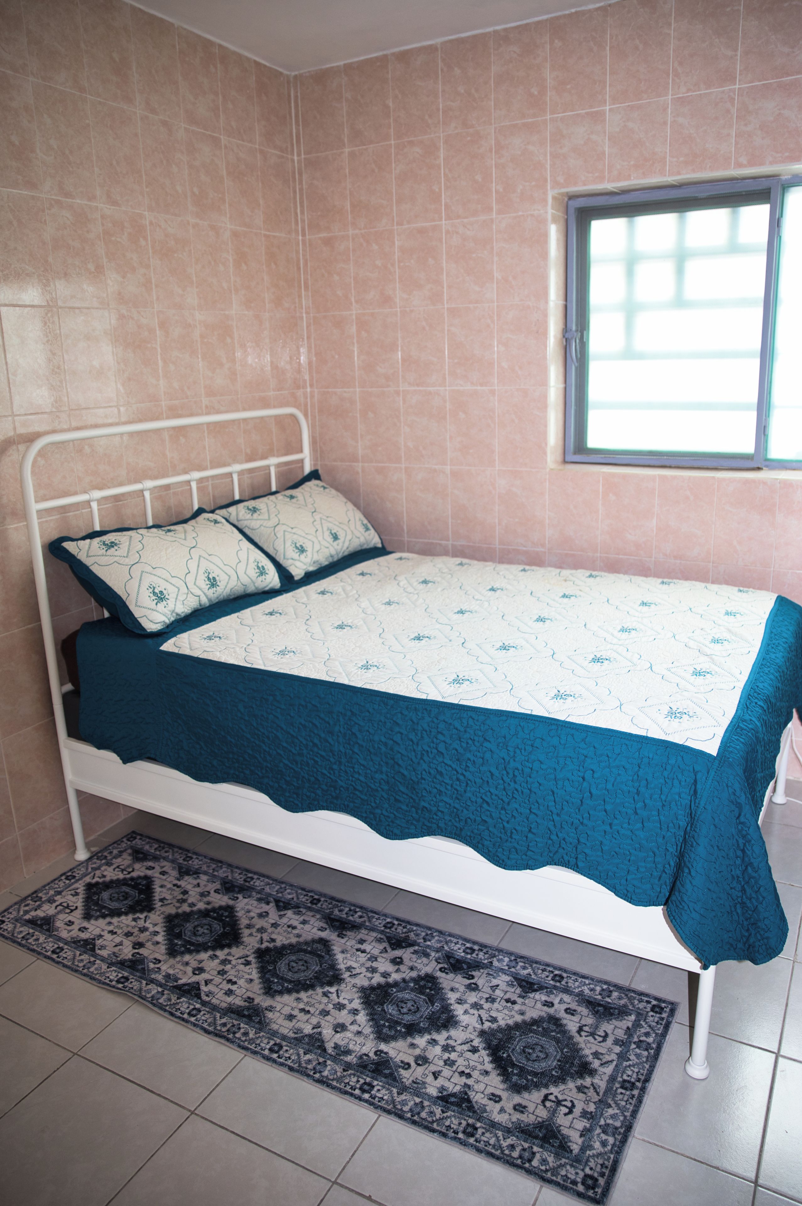 A bedroom with a bed, a window, and a patterned rug.