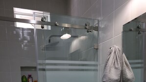 Une salle de bain moderne avec une douche à parois de verre, un lavabo blanc et un miroir sur lequel est accrochée une serviette.