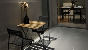 Un espace patio avec une table et des chaises, un vase rempli de fleurs et une fenêtre.
