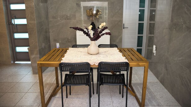 Un coin repas avec une table en bois, des chaises noires et un vase rempli de fleurs.