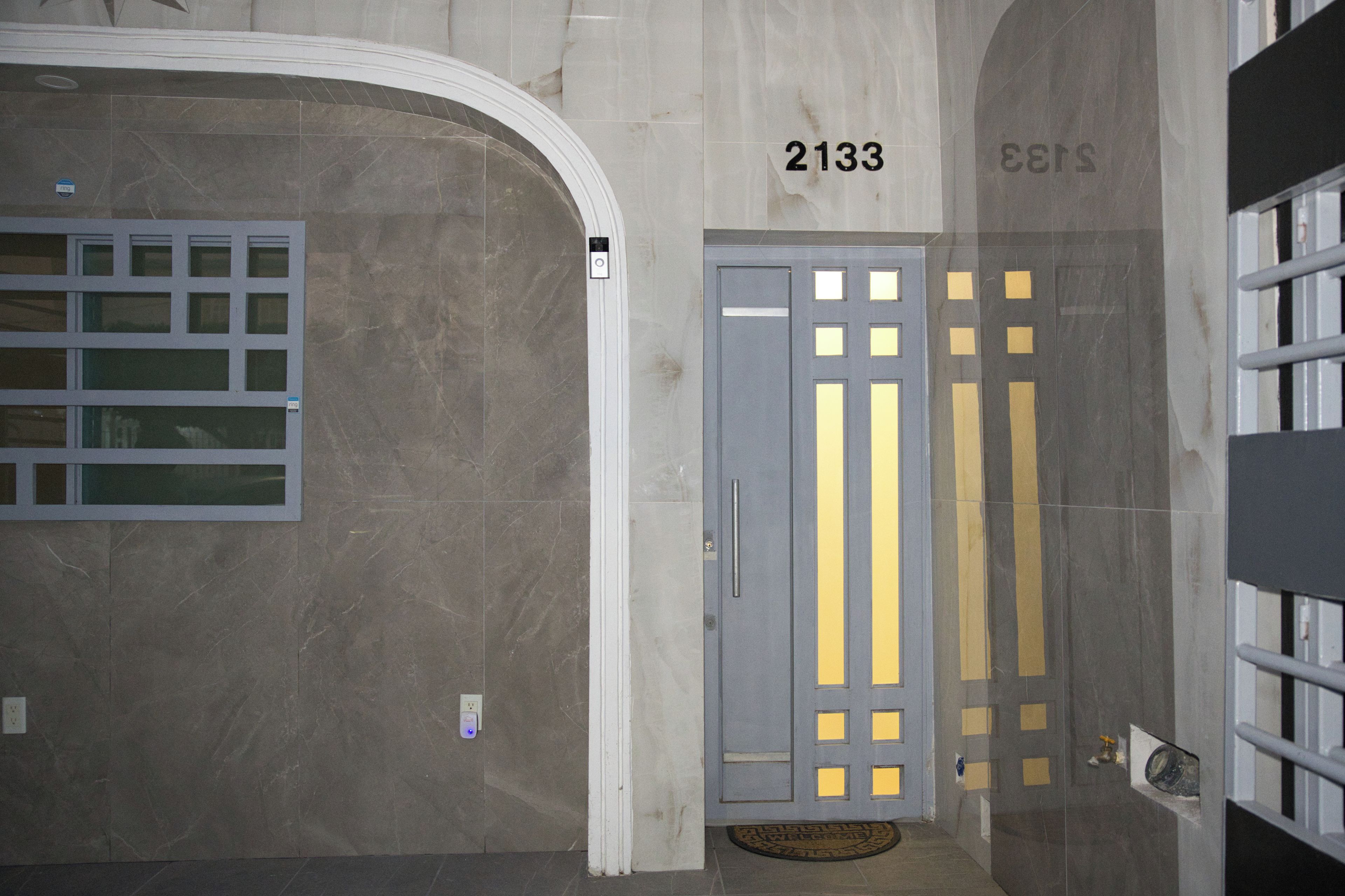 A hallway with a grey door marked with the number 2133, a window with a grid pattern, and a door with vertical blinds.