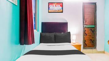 A hotel room with a bed, a nightstand, a lamp, a painting, and a door.