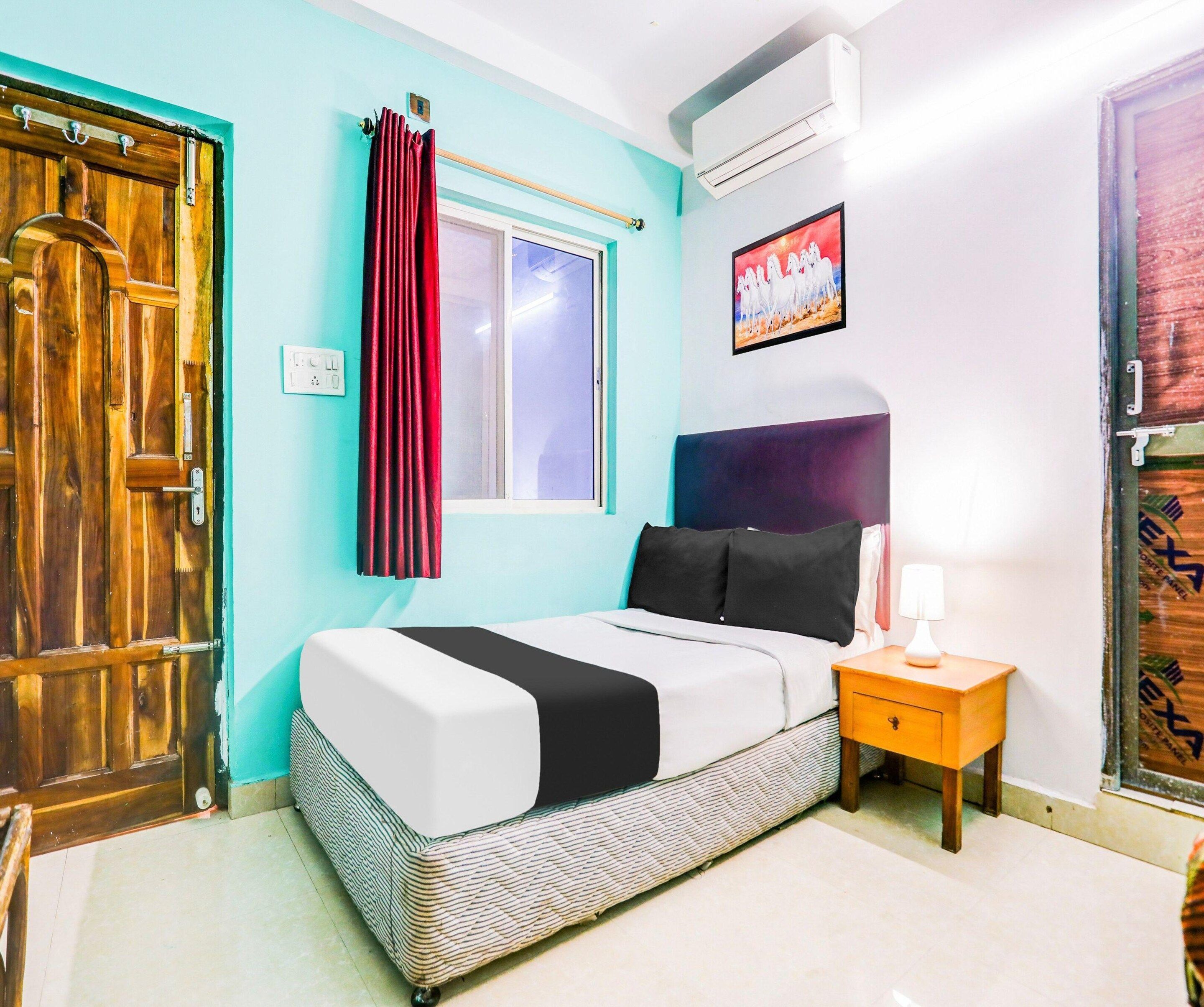 A bedroom with a bed, a nightstand, a window with curtains, an air conditioner, and a door.