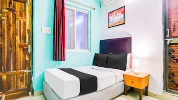 A bedroom with a bed, a nightstand, a window with curtains, an air conditioner, and a door.