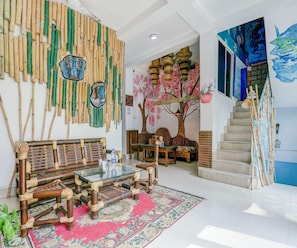 Una habitación con pared de bambú tradicional, un conjunto de sofás, una mesa de centro de vidrio, una escalera y un cuadro.