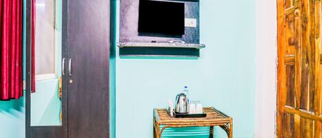 Una habitación con armario, televisor montado en la pared y una mesita con hervidor y tazas.