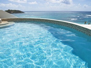 En klarblå pool med en böjd kant, en kant av kakel och utsikt över havet.