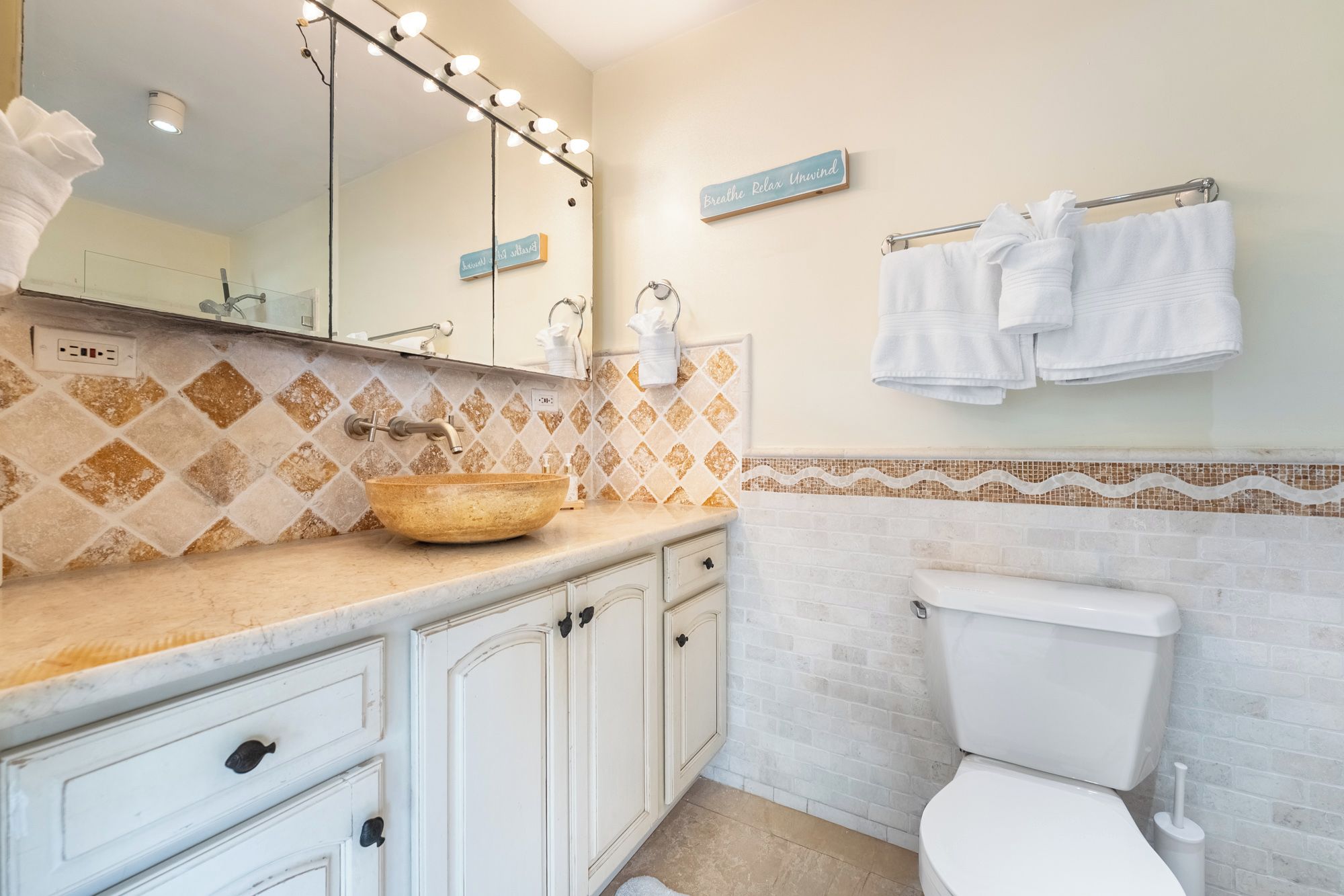 A bathroom with a vanity, a sink, a mirror with lights, a toilet, and towels hanging on a rack.