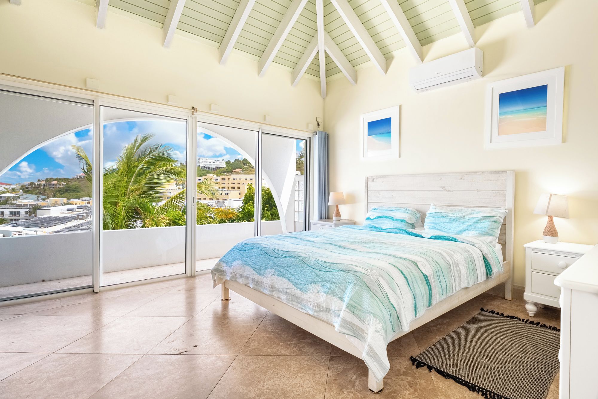 A bedroom with a bed, a nightstand, a lamp, a view through a large window, and a ceiling fan.