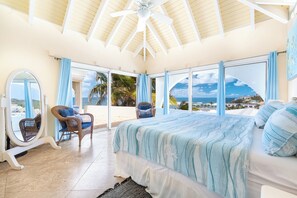 A bedroom with a large bed, a ceiling fan, and a view of the sea. - Villa Oyster Pearl: Concierge Hot Tub Beach Access (Oyster Pond)