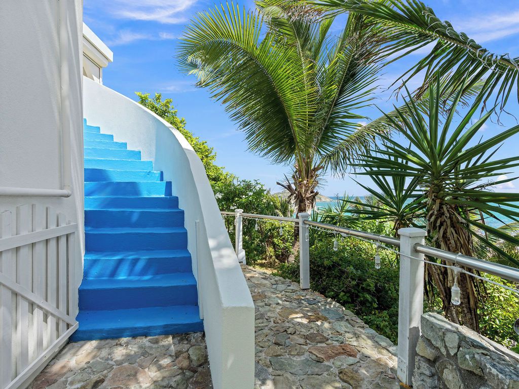 A staircase with blue steps leading up to a white building, surrounded by greenery and a clear sky.