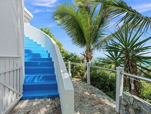 A staircase with blue steps leading up to a white building, surrounded by greenery and a clear sky. - Villa Oyster Pearl: Concierge Hot Tub Beach Access (Oyster Pond)