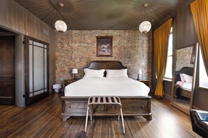 Une chambre avec un mur en briques, un grand lit, une échelle, un miroir et deux lampes suspendues.
