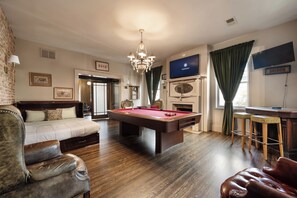 Une pièce comprenant une table de billard, un canapé, un fauteuil en cuir, un lustre, une cheminée et un téléviseur.