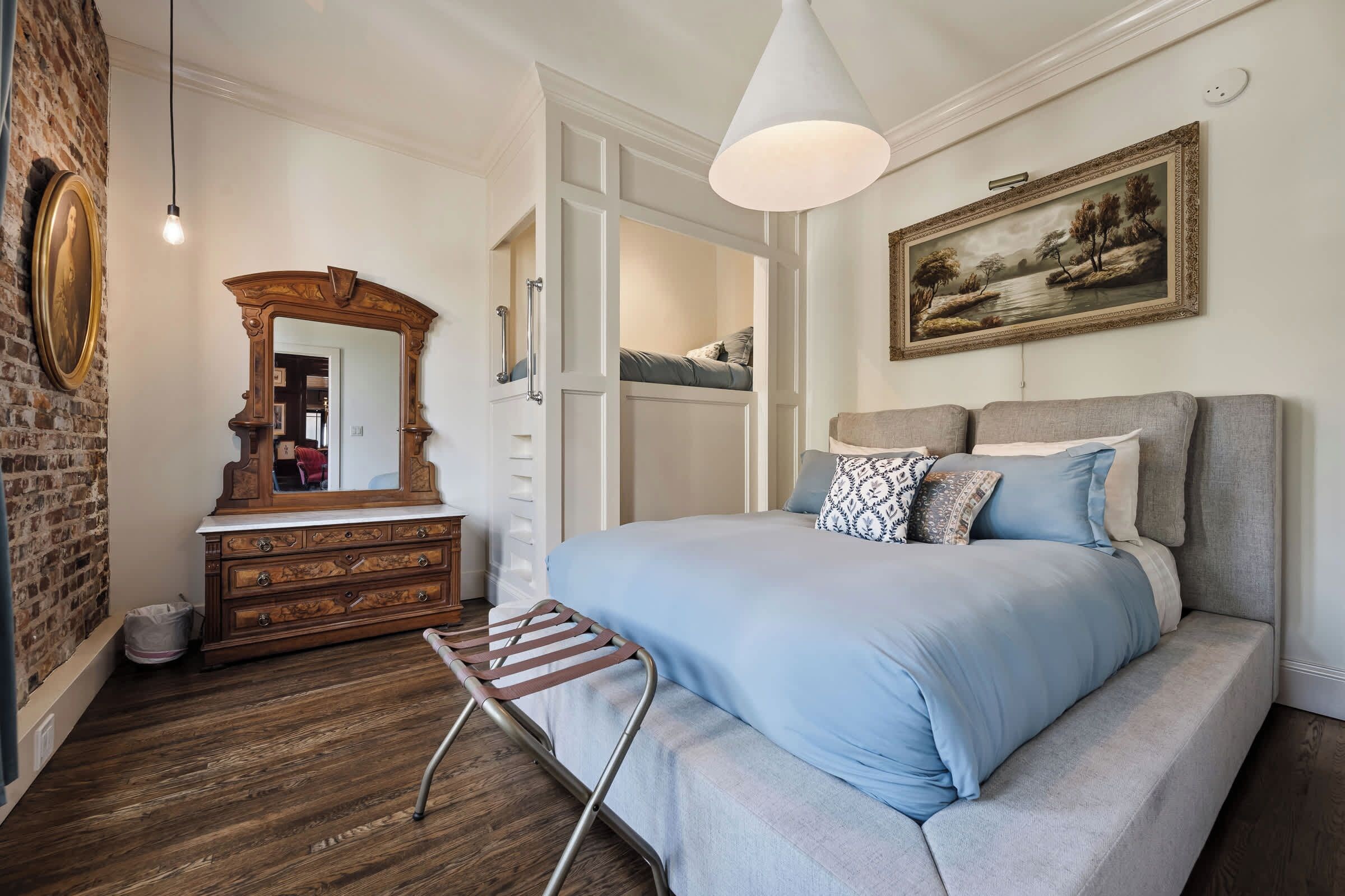 Une chambre à coucher avec un lit, une commode, un miroir, une lampe suspendue et un tableau au mur.