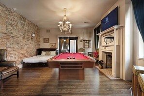 Una habitación con mesa de billar, pared de ladrillo, cama y chimenea.