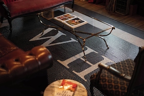 Ein Zimmer mit einem Ledersofa, einem Couchtisch mit Zeitschriften und einem Teppich mit einem Muster, auf dem das Wort 'WIND' steht.