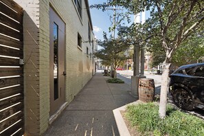 Une rue étroite en milieu urbain, bordée d’un trottoir, d’arbres et de voitures garées.