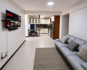 A modern living room with a sofa and a TV mounted on the wall displaying a Netflix advertisement.