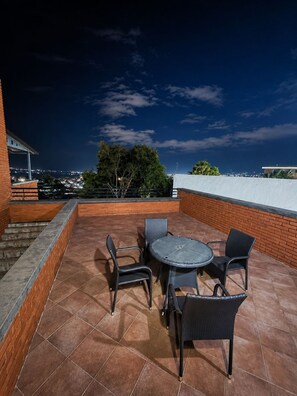 An outdoor patio with a round table and four chairs, a brick wall, and a view of the cityscape at night. - Acogedor&Bello Apto en el Este + Planta Eléctrica (Barquisimeto)