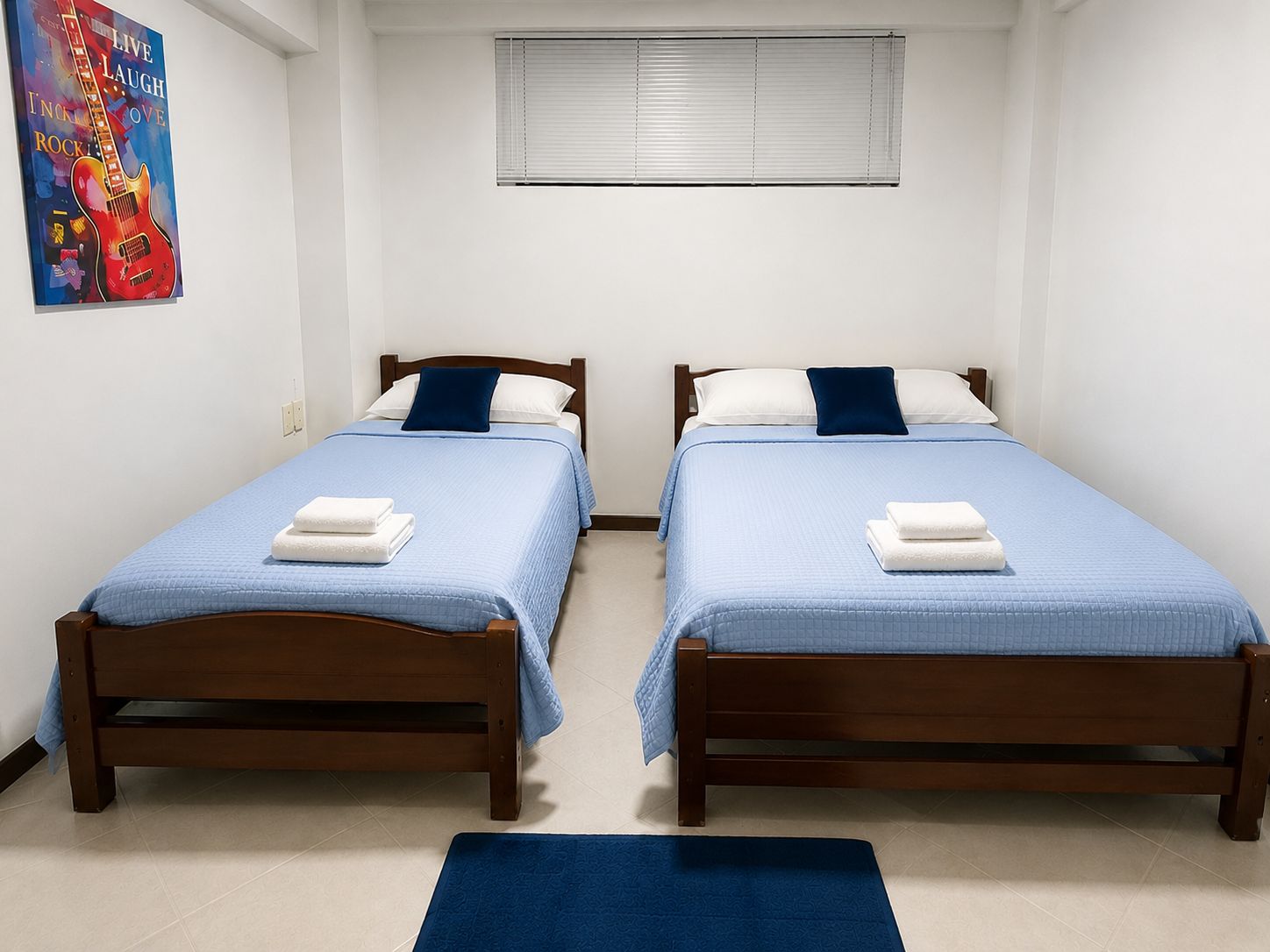 A room with two wooden beds, each with a blue bedspread and white pillows, and a blue rug on the floor.